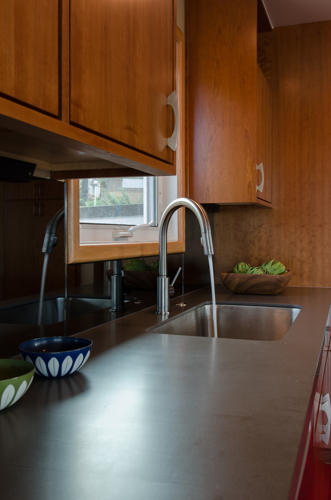 Design ideas for a mid-sized midcentury l-shaped eat-in kitchen in Seattle with a single-bowl sink, flat-panel cabinets, medium wood cabinets, solid surface benchtops, mirror splashback, stainless steel appliances, linoleum floors and with island.