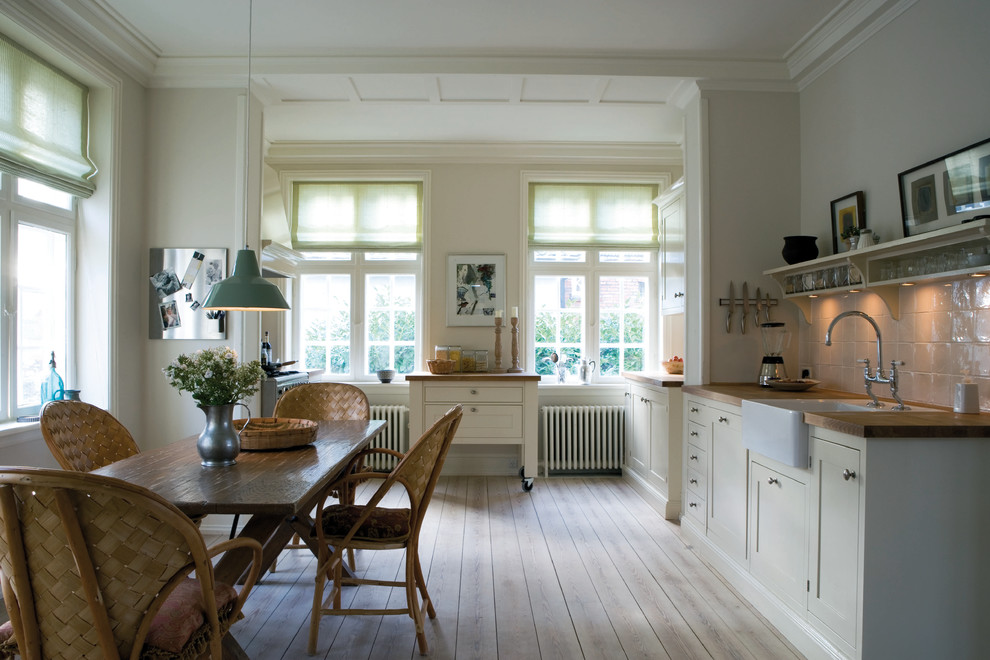 Photo of a mid-sized traditional galley eat-in kitchen in Dorset with a farmhouse sink, white splashback, ceramic splashback and light hardwood floors.