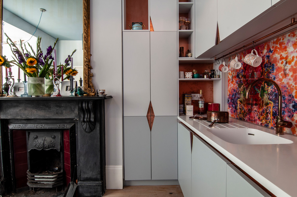 Inspiration for a small eclectic galley eat-in kitchen in London with an integrated sink, flat-panel cabinets, grey cabinets, solid surface benchtops, multi-coloured splashback, glass sheet splashback, coloured appliances, medium hardwood floors, no island, brown floor and white benchtop.