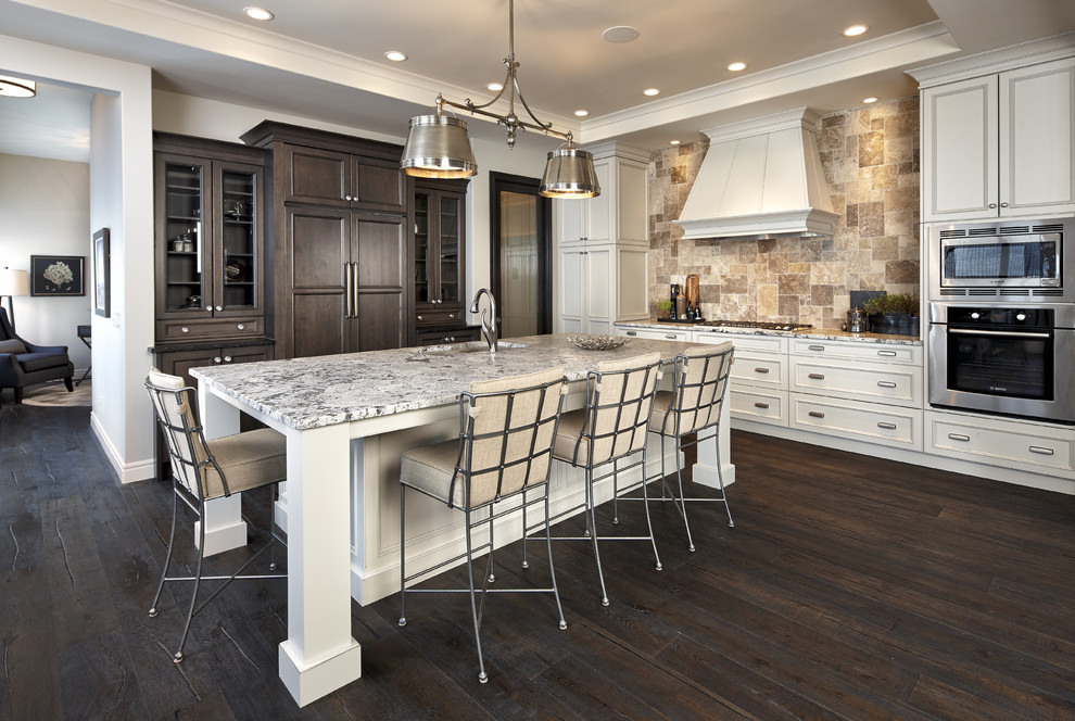 Example of a transitional galley dark wood floor open concept kitchen design in Calgary with an undermount sink, recessed-panel cabinets, white cabinets, granite countertops, beige backsplash, stone tile backsplash, stainless steel appliances and an island