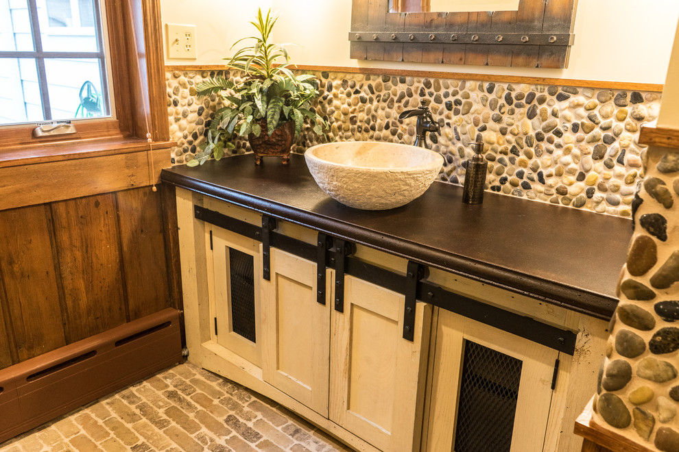 This is an example of a mid-sized country bathroom in Other with shaker cabinets, beige cabinets, beige tile, pebble tile, beige walls, brick floors, a vessel sink, concrete benchtops and multi-coloured floor.