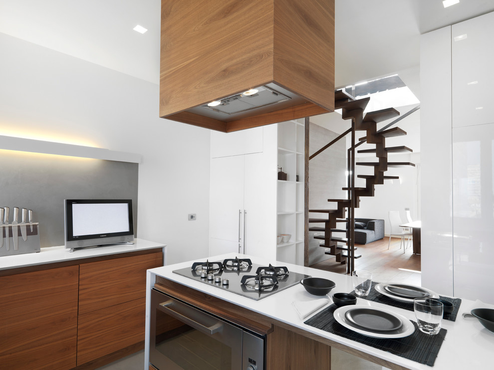 This is an example of a mid-sized contemporary open plan kitchen in Milan with flat-panel cabinets, medium wood cabinets, solid surface benchtops, stainless steel appliances, light hardwood floors and with island.