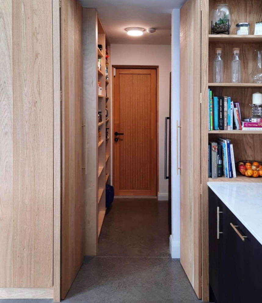 Inspiration for a medium sized modern galley separated utility room in Dublin with a built-in sink, flat-panel cabinets, light wood cabinets, concrete worktops, concrete flooring, a concealed washer and dryer, grey floors, black worktops, a vaulted ceiling and panelled walls.