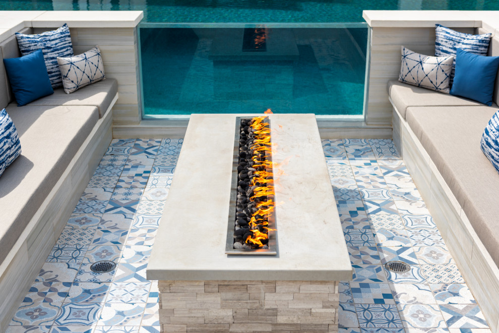 Modelo de piscina infinita contemporánea grande a medida en patio trasero con paisajismo de piscina y suelo de baldosas
