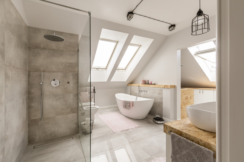 This is an example of a large contemporary grey and white bathroom in London with a freestanding bath, a one-piece toilet, grey tiles, ceramic tiles, ceramic flooring, wooden worktops, grey floors, a built-in shower, grey walls, a vessel sink, an open shower and beige worktops.