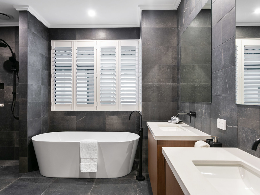 This is an example of a mid-sized modern master bathroom in Perth with recessed-panel cabinets, medium wood cabinets, a freestanding tub, an open shower, gray tile, ceramic tile, grey walls, ceramic floors, an integrated sink, tile benchtops, grey floor, an open shower and white benchtops.