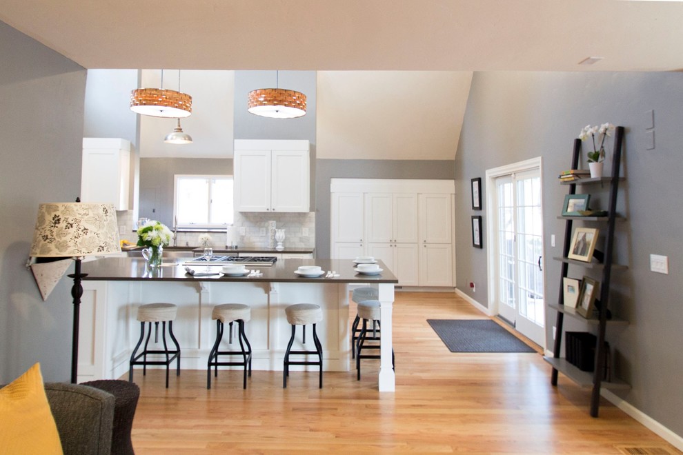 Design ideas for an expansive transitional l-shaped eat-in kitchen in Denver with a farmhouse sink, shaker cabinets, white cabinets, quartz benchtops, white splashback, stone tile splashback, stainless steel appliances, light hardwood floors and with island.