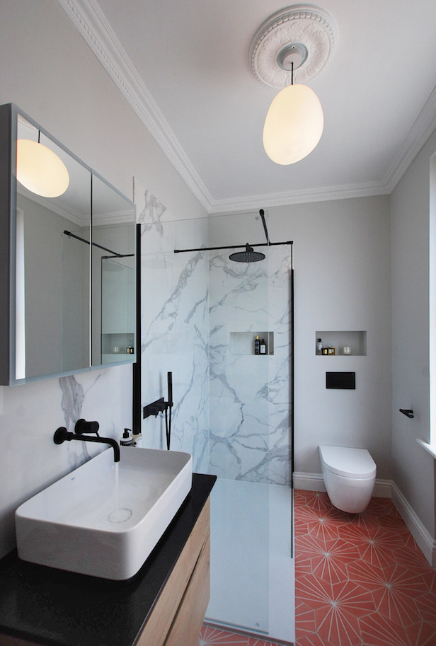 Photo of a small modern 3/4 bathroom in London with light wood cabinets, an open shower, a wall-mount toilet, porcelain tile, grey walls, terra-cotta floors, a vessel sink, marble benchtops, pink floor, an open shower, black benchtops and multi-coloured tile.