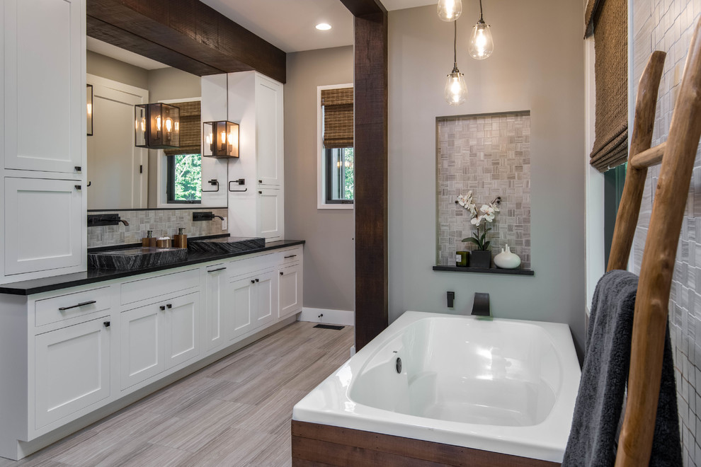 Inspiration for a mid-sized country master bathroom in Other with shaker cabinets, white cabinets, a freestanding tub, an alcove shower, a two-piece toilet, beige tile, mosaic tile, beige walls, porcelain floors, a trough sink, soapstone benchtops, beige floor and black benchtops.