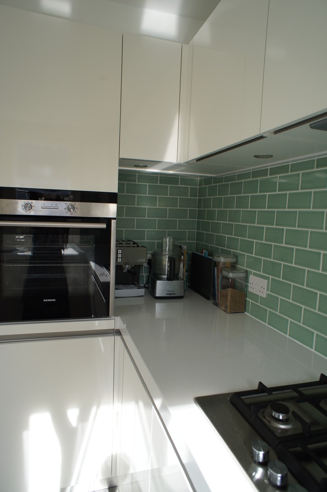 Mid-sized contemporary u-shaped open plan kitchen in London with a single-bowl sink, flat-panel cabinets, white cabinets, solid surface benchtops, green splashback, subway tile splashback, coloured appliances, ceramic floors and no island.