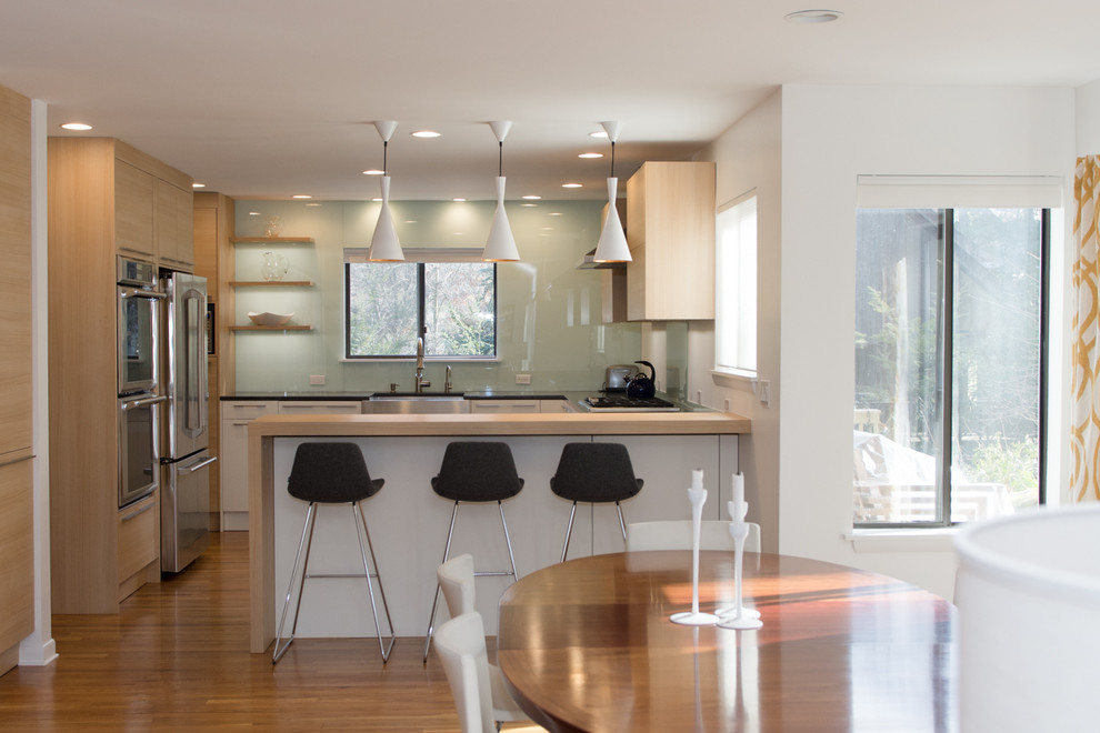 Photo of a mid-sized modern u-shaped eat-in kitchen in New York with an undermount sink, flat-panel cabinets, light wood cabinets, solid surface benchtops, blue splashback, glass sheet splashback, stainless steel appliances, medium hardwood floors and a peninsula.