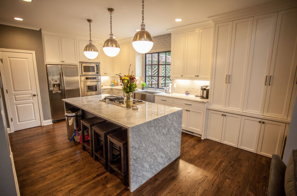 Mid-sized transitional u-shaped dark wood floor and brown floor eat-in kitchen photo in Atlanta with a farmhouse sink, recessed-panel cabinets, white cabinets, marble countertops, gray backsplash, subway tile backsplash, stainless steel appliances, an island and white countertops