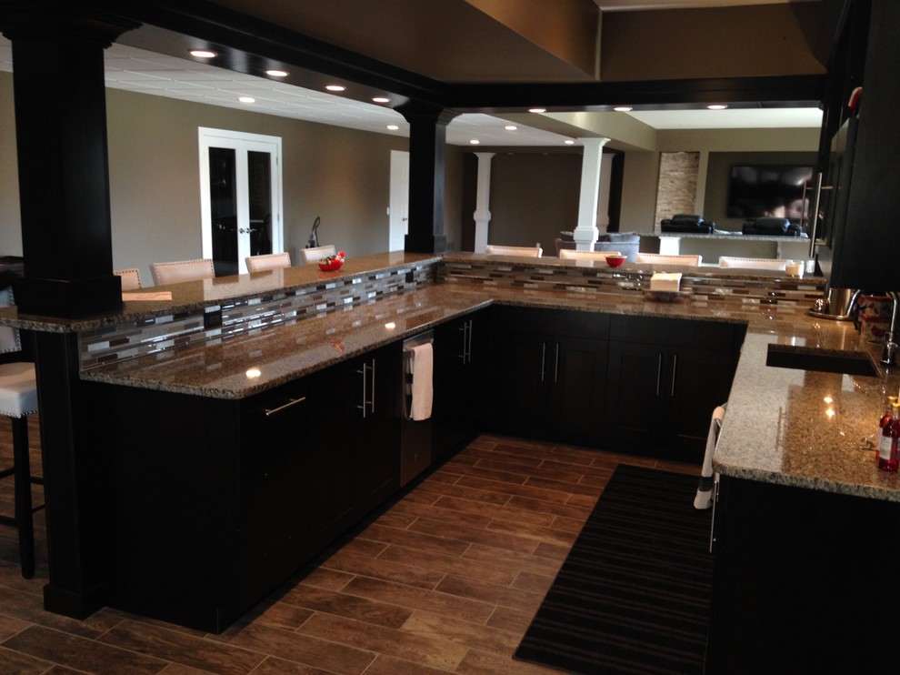 This is an example of a large arts and crafts u-shaped seated home bar in Detroit with an undermount sink, shaker cabinets, dark wood cabinets, granite benchtops, multi-coloured splashback and porcelain floors.
