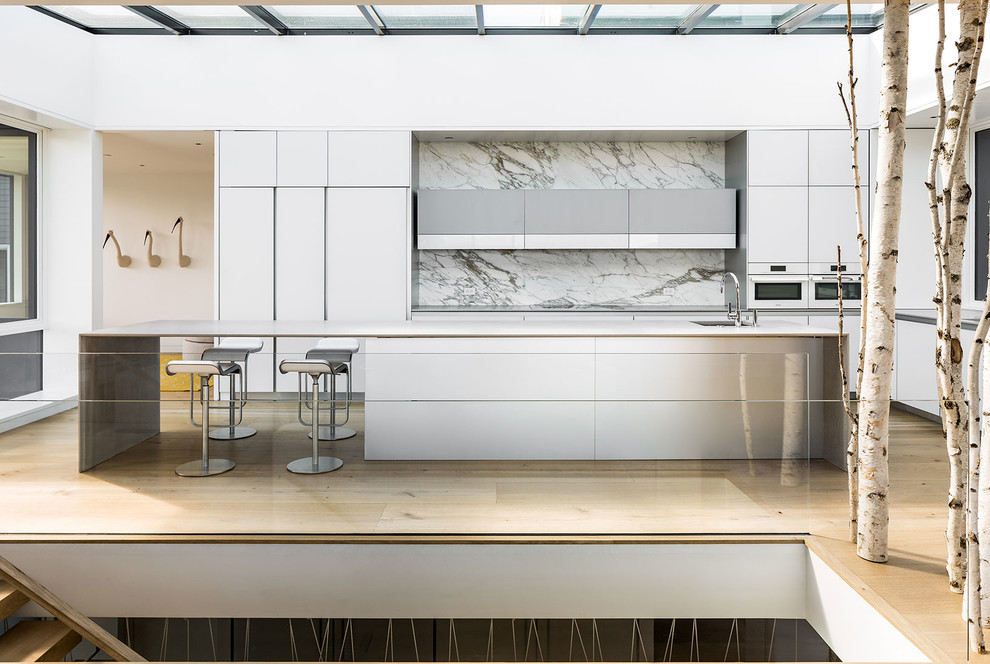 Photo of a large midcentury l-shaped eat-in kitchen in San Francisco with flat-panel cabinets, white cabinets, concrete benchtops, white splashback, marble splashback, white appliances, light hardwood floors and with island.