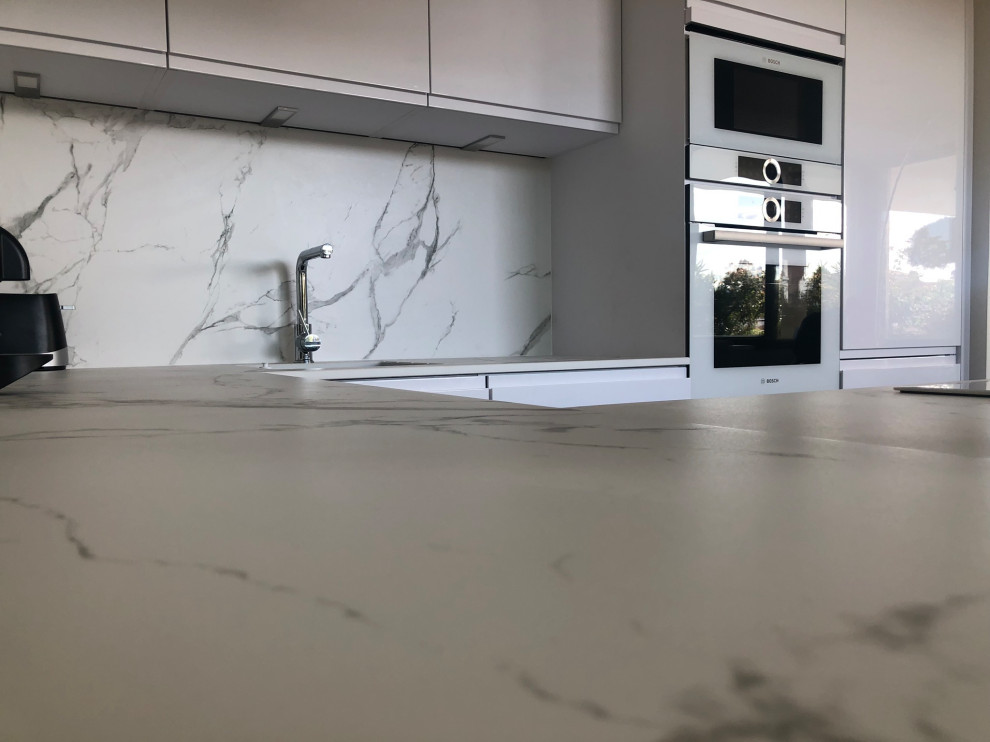 Inspiration for a mid-sized contemporary u-shaped eat-in kitchen in Lyon with an integrated sink, white cabinets, quartzite benchtops, white splashback, stone slab splashback, stainless steel appliances, dark hardwood floors, brown floor and white benchtop.