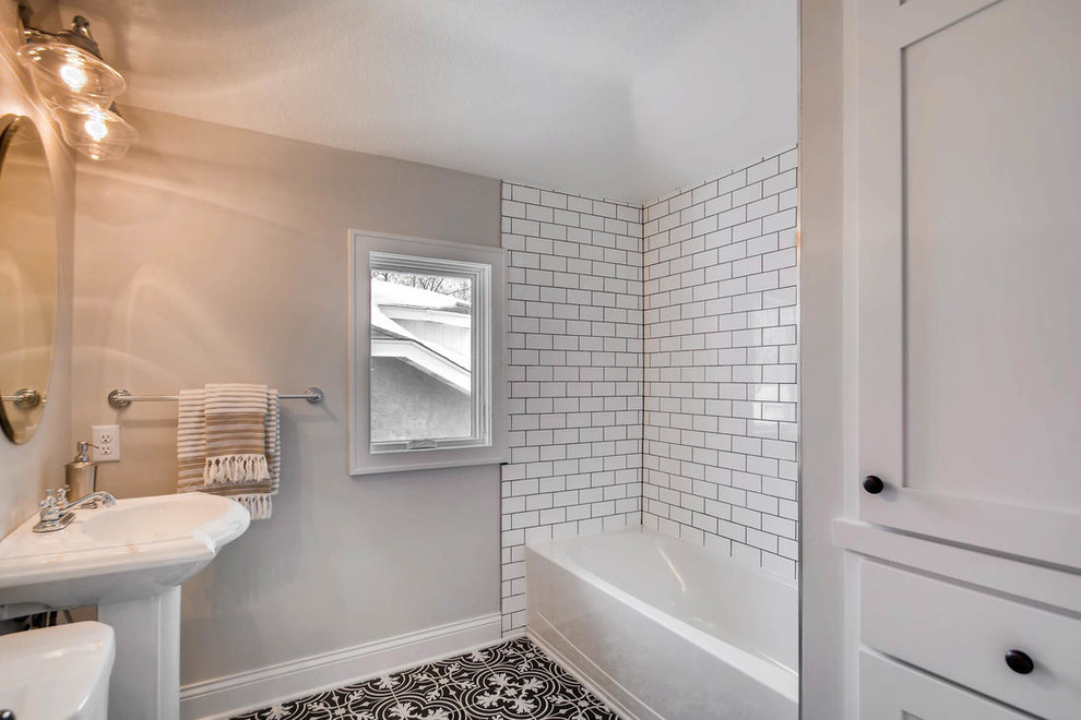 Example of a mid-sized transitional white tile and subway tile porcelain tile and black floor drop-in bathtub design in Minneapolis with a one-piece toilet, gray walls and a pedestal sink