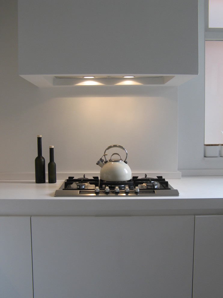 This is an example of a mid-sized contemporary u-shaped separate kitchen in Cheshire with a double-bowl sink, white cabinets, white splashback, stainless steel appliances and no island.