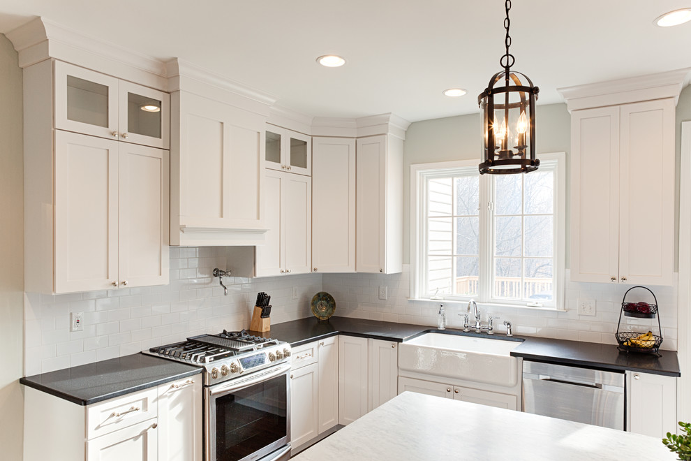 This is an example of a large transitional u-shaped eat-in kitchen in Philadelphia with a farmhouse sink, shaker cabinets, white cabinets, granite benchtops, white splashback, subway tile splashback, stainless steel appliances, with island and medium hardwood floors.