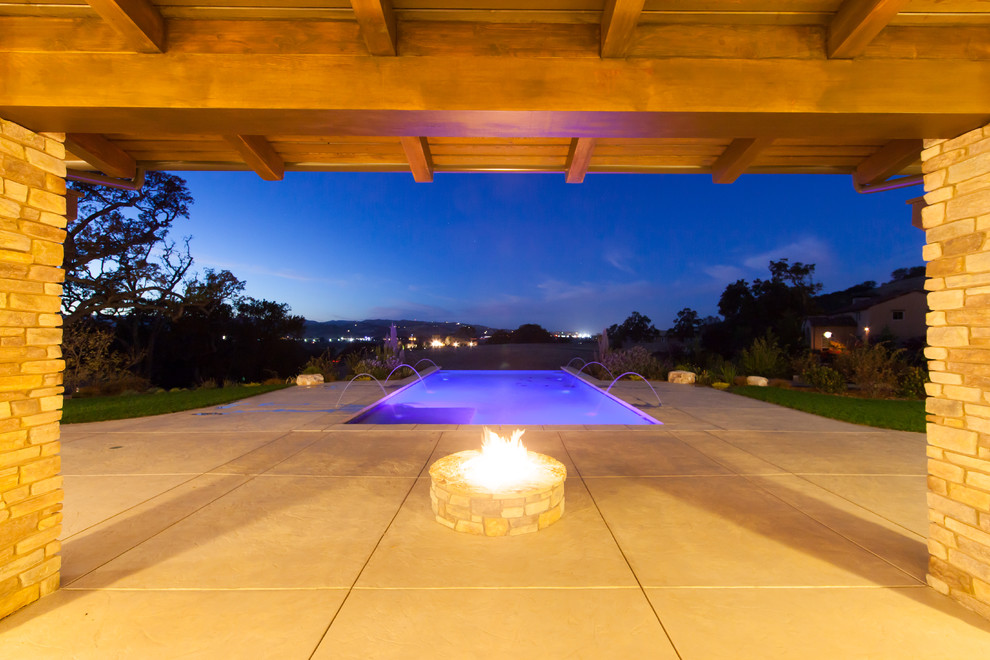 Photo of a large mediterranean backyard rectangular pool in San Luis Obispo with a water feature and stamped concrete.