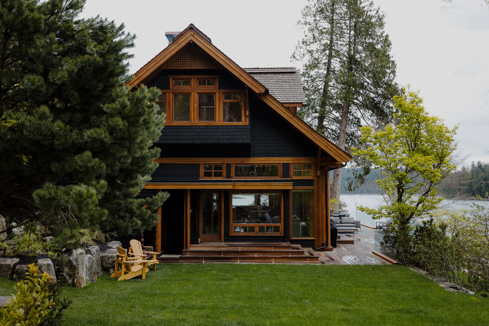 Стильный дизайн: огромный, трехэтажный, деревянный, черный частный загородный дом в стиле кантри с крышей из гибкой черепицы, коричневой крышей и отделкой дранкой - последний тренд