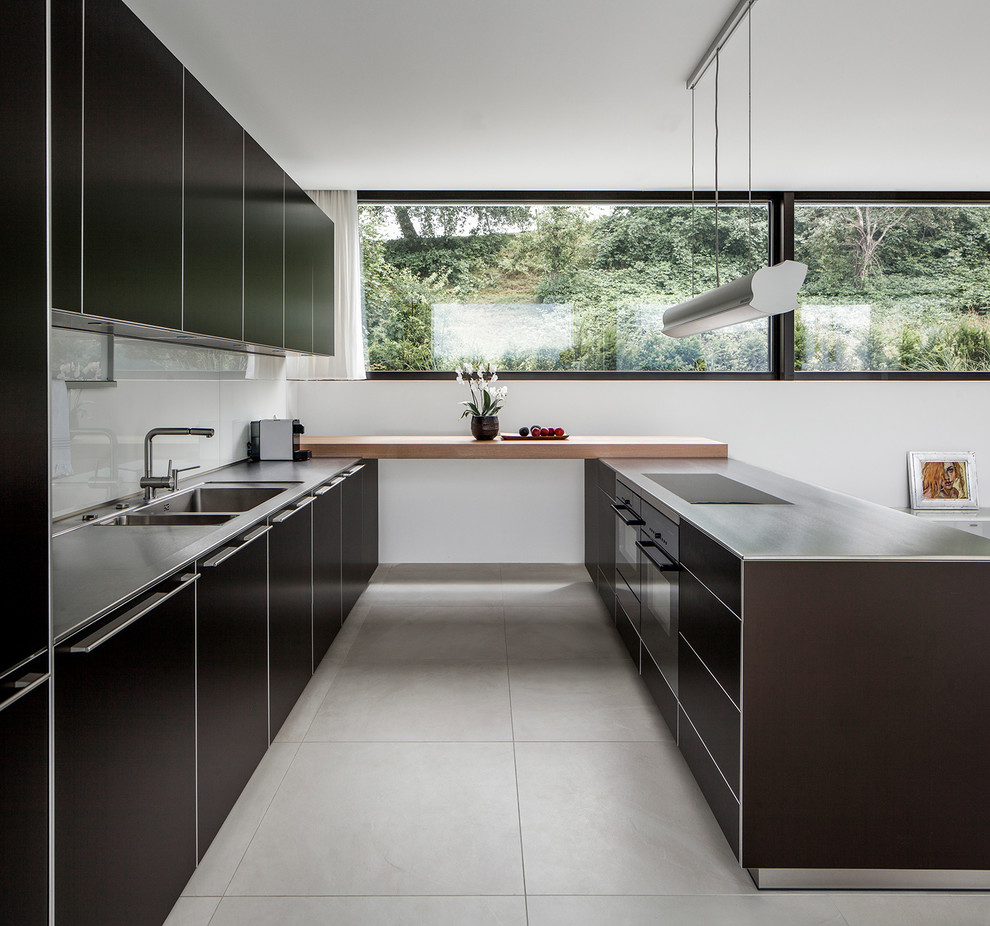 This is an example of an expansive contemporary galley open plan kitchen in Other with a double-bowl sink, flat-panel cabinets, wood benchtops, white splashback, glass tile splashback, brown benchtop, black cabinets, black appliances, a peninsula and grey floor.
