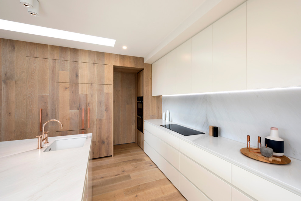 Photo of a contemporary galley kitchen in Melbourne with an undermount sink, flat-panel cabinets, white cabinets, white splashback, light hardwood floors and with island.