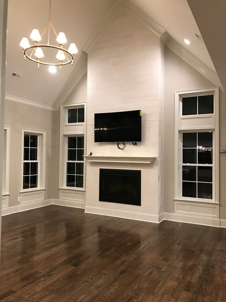 Design ideas for a mid-sized traditional open concept family room in Raleigh with grey walls, dark hardwood floors, a standard fireplace, a wood fireplace surround, a wall-mounted tv and brown floor.