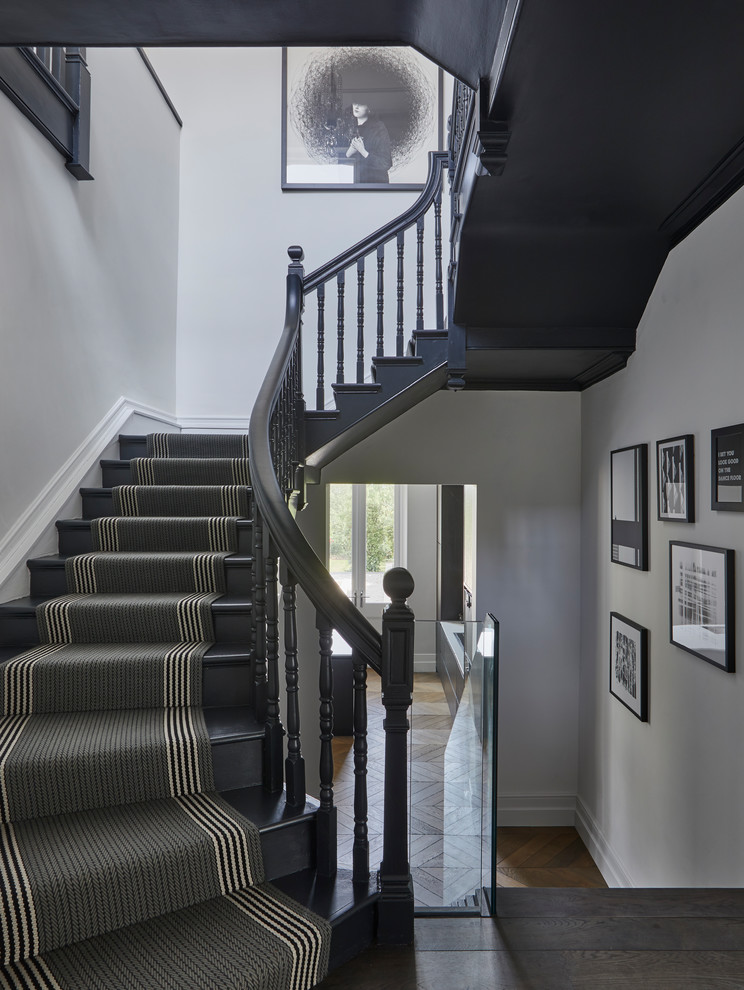 This is an example of a mid-sized transitional carpeted u-shaped staircase in Hertfordshire with carpet risers and wood railing.