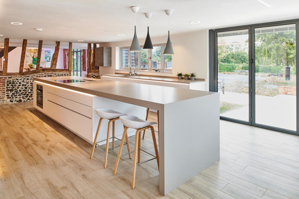 Photo of a large contemporary single-wall open plan kitchen in Hertfordshire with flat-panel cabinets, grey cabinets, black appliances, an island, beige floors and grey worktops.