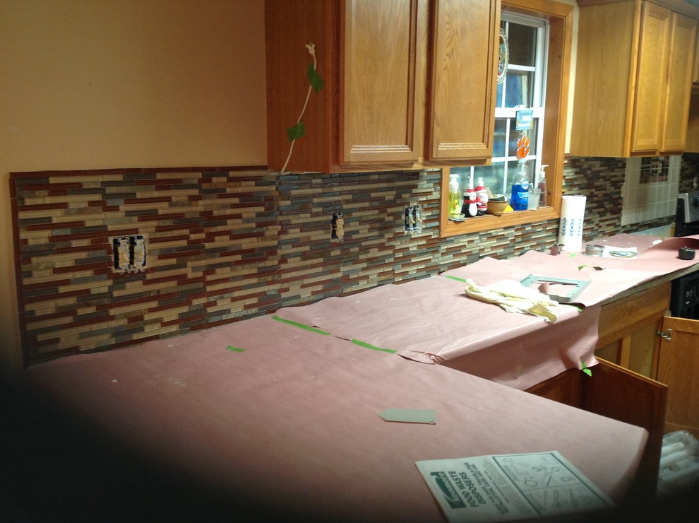 Example of a l-shaped eat-in kitchen design with an undermount sink, flat-panel cabinets, brown backsplash, glass tile backsplash, stainless steel appliances and a peninsula