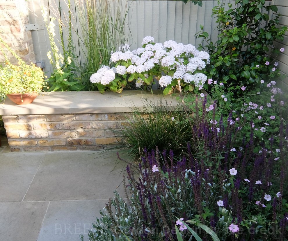 This is an example of a small country courtyard garden in London with natural stone pavers.