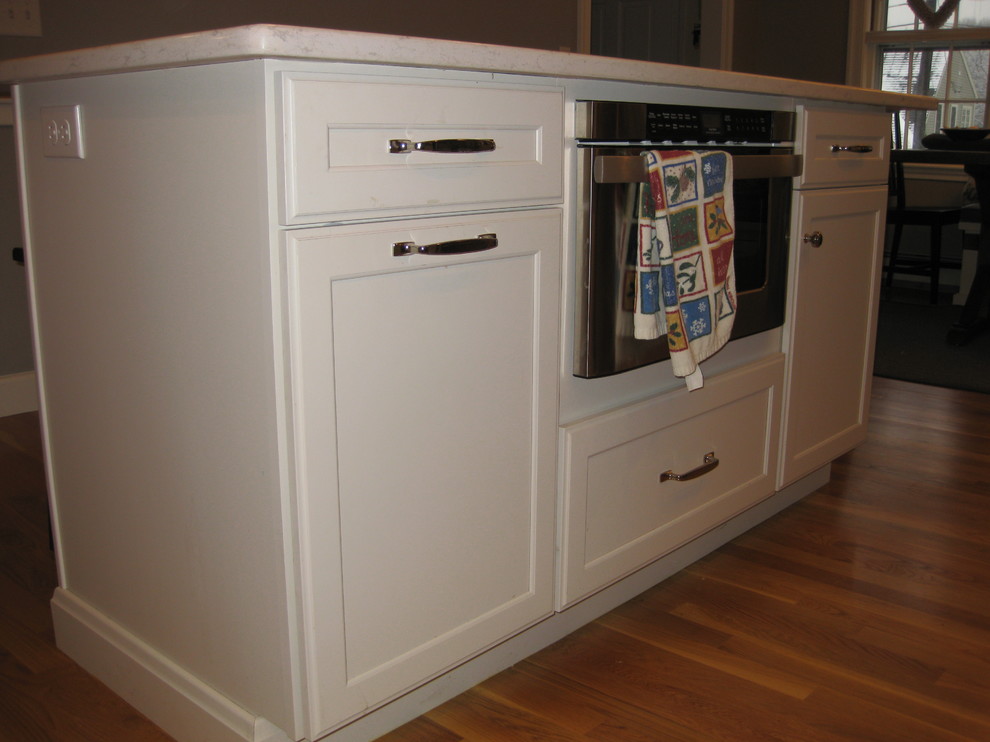 Example of a transitional l-shaped medium tone wood floor eat-in kitchen design in Boston with an undermount sink, white cabinets, quartz countertops, stainless steel appliances, an island, shaker cabinets, green backsplash, subway tile backsplash and black countertops