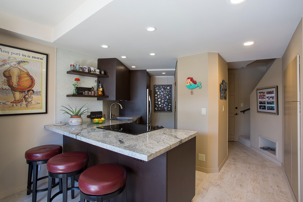 This is an example of a small contemporary l-shaped eat-in kitchen in Hawaii with a single-bowl sink, flat-panel cabinets, dark wood cabinets, granite benchtops, white splashback, glass tile splashback, stainless steel appliances, porcelain floors and a peninsula.
