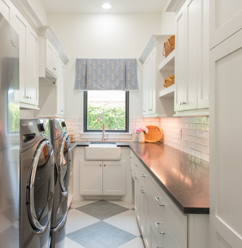 This is an example of a beach style u-shaped dedicated laundry room in Houston with a farmhouse sink, shaker cabinets, white cabinets, white walls, a side-by-side washer and dryer and grey benchtop.