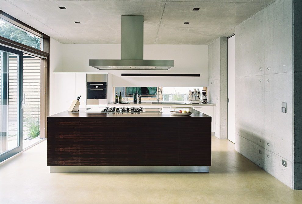Inspiration for a large contemporary open plan kitchen in Nuremberg with an undermount sink, flat-panel cabinets, white cabinets, stainless steel benchtops, panelled appliances, concrete floors, with island and mirror splashback.