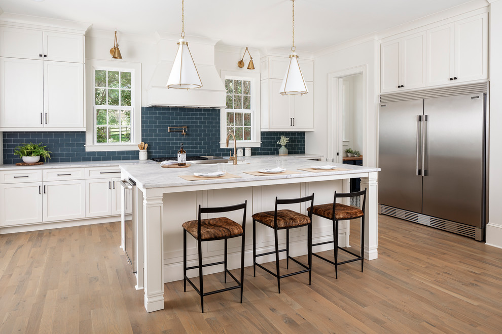 Design ideas for a large transitional l-shaped open plan kitchen in Charlotte with a farmhouse sink, marble benchtops, blue splashback, subway tile splashback, stainless steel appliances, medium hardwood floors, with island and white benchtop.
