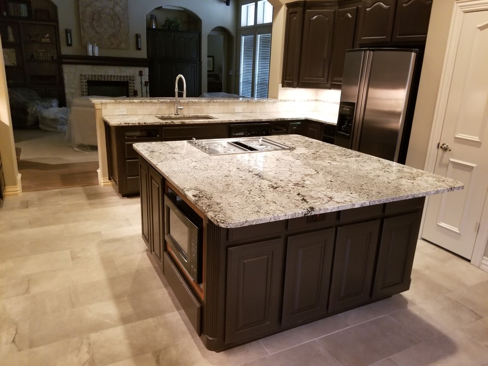 Mid-sized traditional l-shaped open plan kitchen in Dallas with an undermount sink, raised-panel cabinets, dark wood cabinets, granite benchtops, grey splashback, porcelain splashback, stainless steel appliances, porcelain floors, with island, grey floor and grey benchtop.