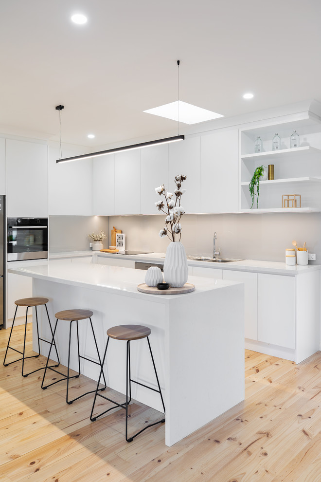 Design ideas for a contemporary l-shaped kitchen pantry in Adelaide with a drop-in sink, flat-panel cabinets, white cabinets, quartz benchtops, grey splashback, glass sheet splashback, stainless steel appliances, light hardwood floors, with island, brown floor and white benchtop.