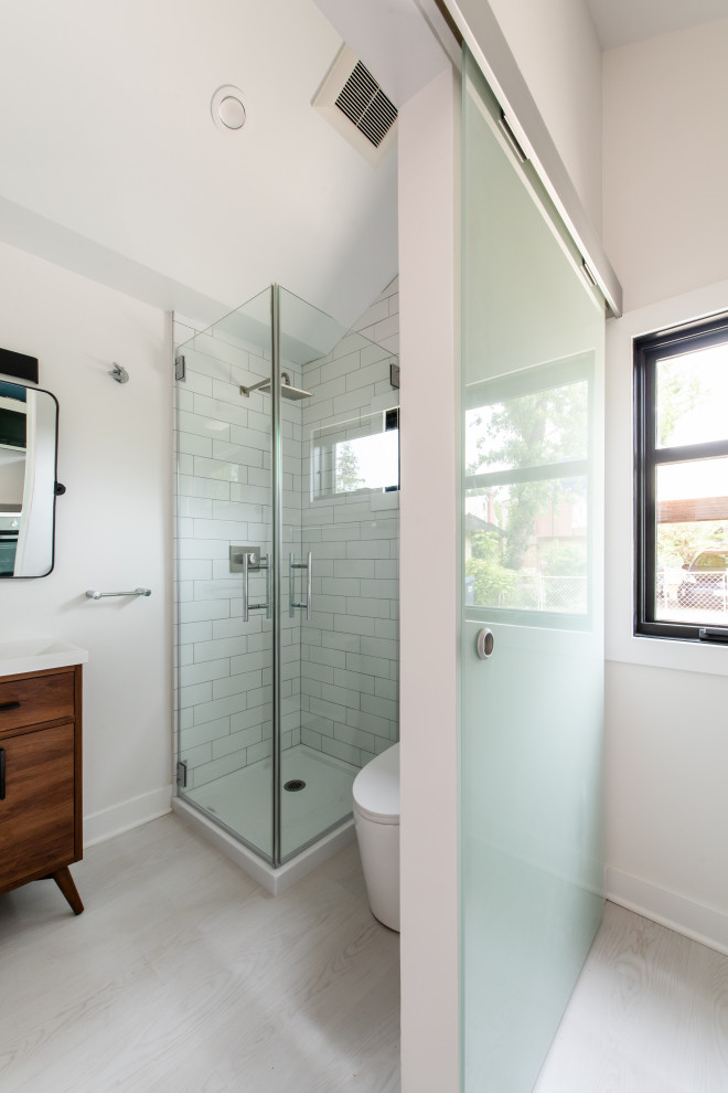 This is an example of a small contemporary 3/4 bathroom in DC Metro with furniture-like cabinets, medium wood cabinets, a corner shower, a one-piece toilet, white tile, subway tile, white walls, linoleum floors, a console sink, grey floor, a hinged shower door, a laundry, a single vanity and a built-in vanity.