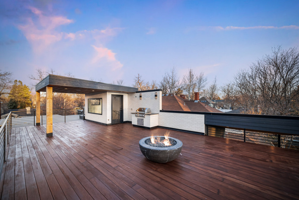 Cette image montre un porche d'entrée de maison arrière urbain avec un foyer extérieur, une terrasse en bois, une extension de toiture et un garde-corps en métal.