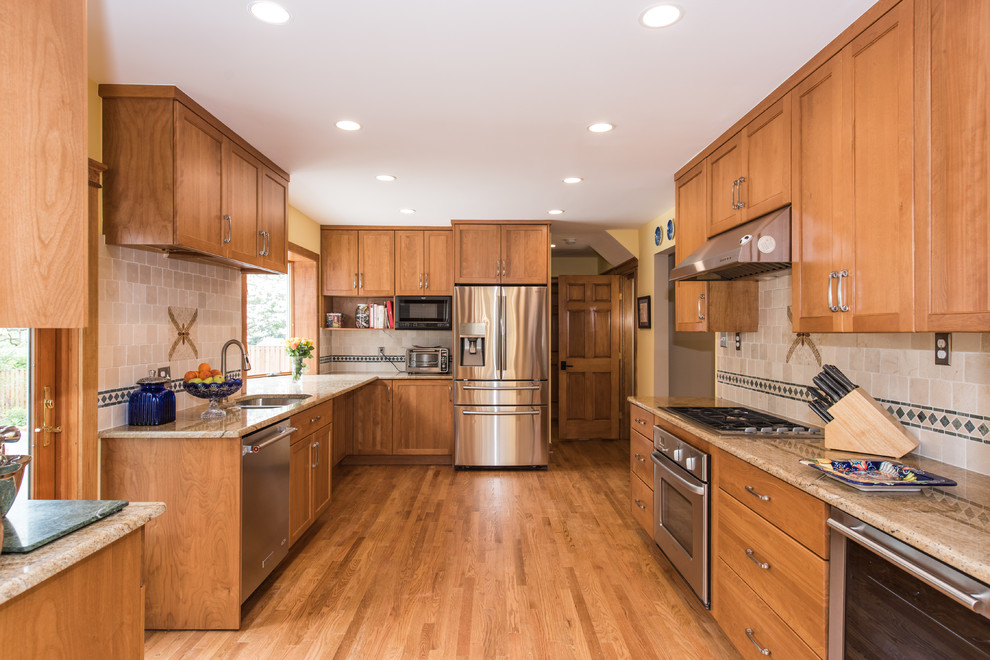 Large arts and crafts u-shaped open plan kitchen in DC Metro with an undermount sink, brown cabinets, granite benchtops, beige splashback, terra-cotta splashback, stainless steel appliances, light hardwood floors, brown floor, beaded inset cabinets and no island.