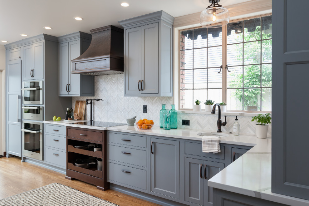 Example of a large transitional l-shaped medium tone wood floor and brown floor kitchen design in Seattle with an undermount sink, shaker cabinets, gray cabinets, gray backsplash, paneled appliances and white countertops