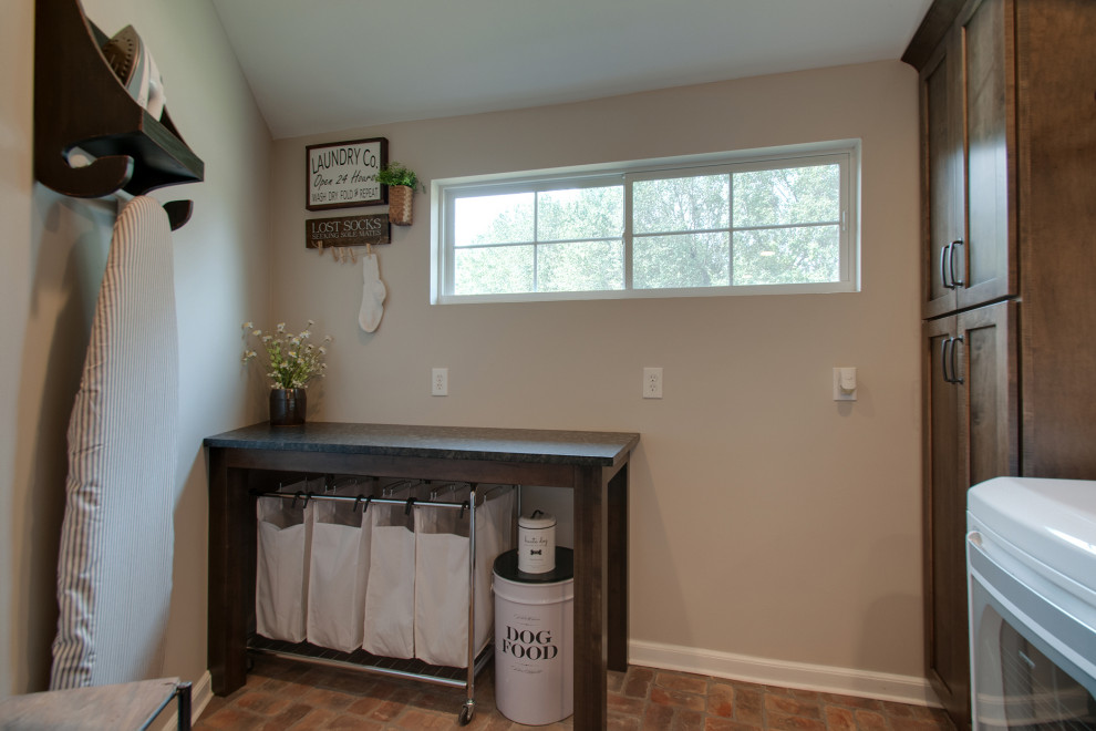 Small country utility room in Nashville with a farmhouse sink, shaker cabinets, brown cabinets, granite benchtops, grey walls, brick floors, a side-by-side washer and dryer, multi-coloured floor and black benchtop.