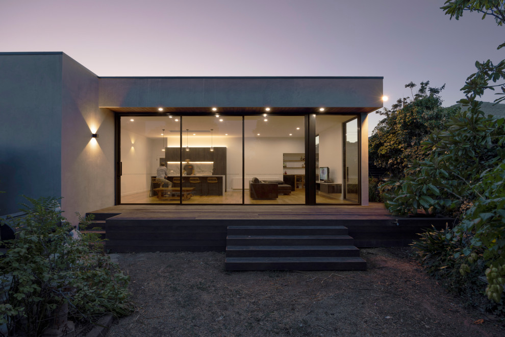 Medium sized and gey modern bungalow detached house in Melbourne with concrete fibreboard cladding, a metal roof, a black roof and board and batten cladding.