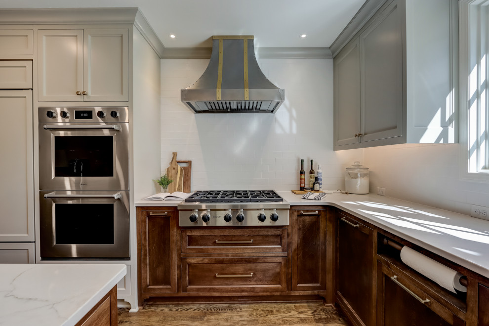 Inspiration for a mid-sized transitional l-shaped medium tone wood floor and brown floor enclosed kitchen remodel in Milwaukee with an undermount sink, recessed-panel cabinets, medium tone wood cabinets, quartz countertops, white backsplash, ceramic backsplash, stainless steel appliances, an island and white countertops