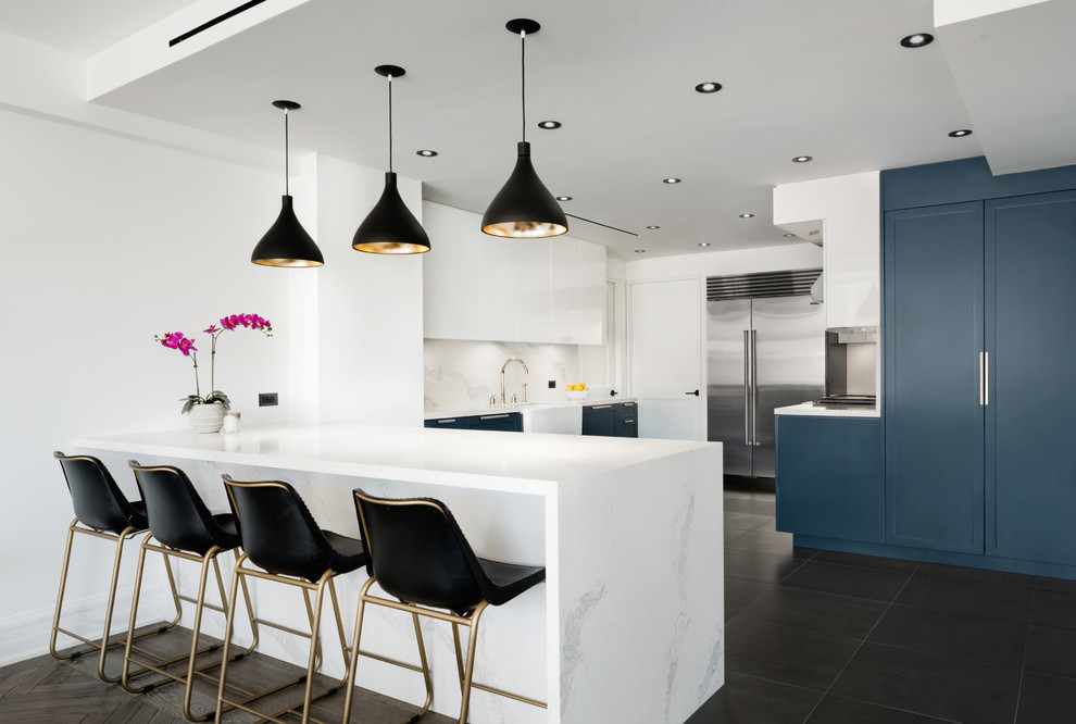 Contemporary kitchen in New York with a farmhouse sink, shaker cabinets, white splashback, stainless steel appliances, a peninsula and brown floor.