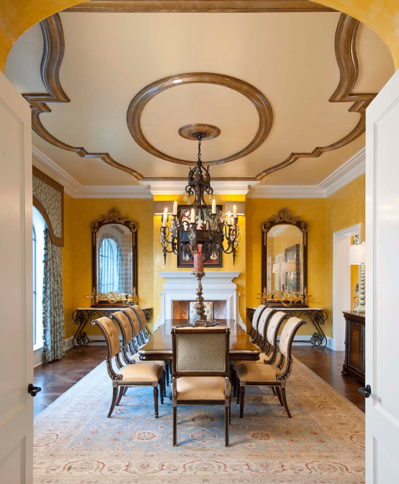 Large mediterranean separate dining room in Los Angeles with yellow walls, medium hardwood floors, a standard fireplace, a plaster fireplace surround and brown floor.