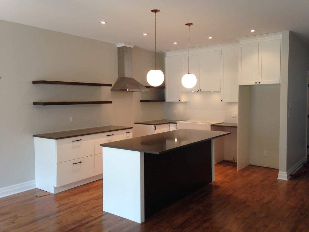 This is an example of a mid-sized contemporary l-shaped eat-in kitchen in Montreal with a farmhouse sink, shaker cabinets, white cabinets, quartz benchtops, stainless steel appliances, medium hardwood floors and with island.