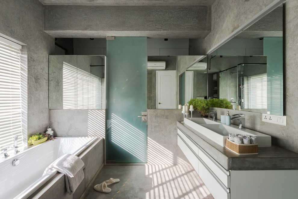 Photo of an industrial master bathroom in Ahmedabad with flat-panel cabinets, white cabinets, a drop-in tub, grey walls, concrete floors, a trough sink, grey floor and grey benchtops.
