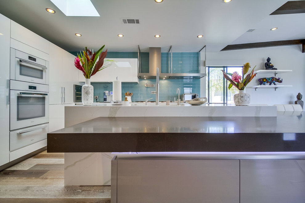 Large contemporary l-shaped open plan kitchen in San Diego with an undermount sink, flat-panel cabinets, white cabinets, quartz benchtops, blue splashback, glass tile splashback, stainless steel appliances, medium hardwood floors and with island.